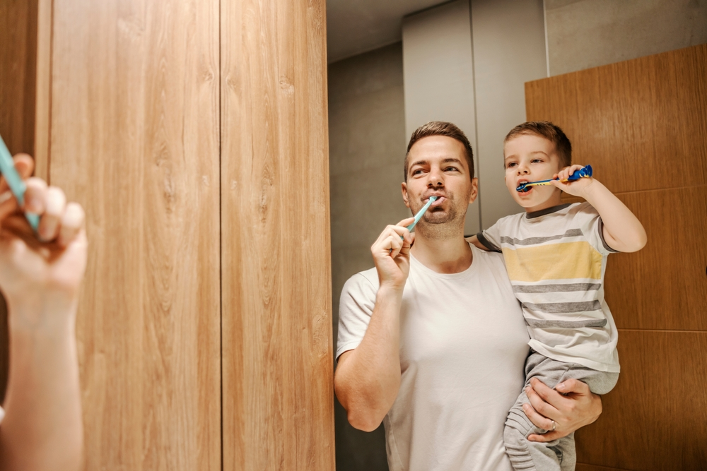 A father and son brushing their teeth together.
